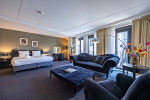 Junior Suite in Amrâth Grand Hotel Frans Hals met twee eenpersoonsbedden, een zwarte stoffen fauteuil, rode bewerkte gordijnen, een spiegel in de hoek van de kamer