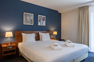 Deluxe kamer in Amrâth Grand Hotel Frans Hals met twee eenpersoonsbedden, nachtlampen, een fauteuil en schilderijen onder een gebogen plafond.