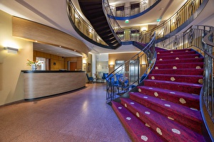 Receptie van het Amrâth Grand Hotel Frans Hals, met een moderne inrichting en warme verlichting en een trap met rode vloerbedekking richting de kamers