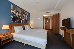 Deluxe kamer in Amrâth Grand Hotel Frans Hals met twee eenpersoonsbedden, nachtlampen, groot schilderij boven het bed en een houten kledingkast