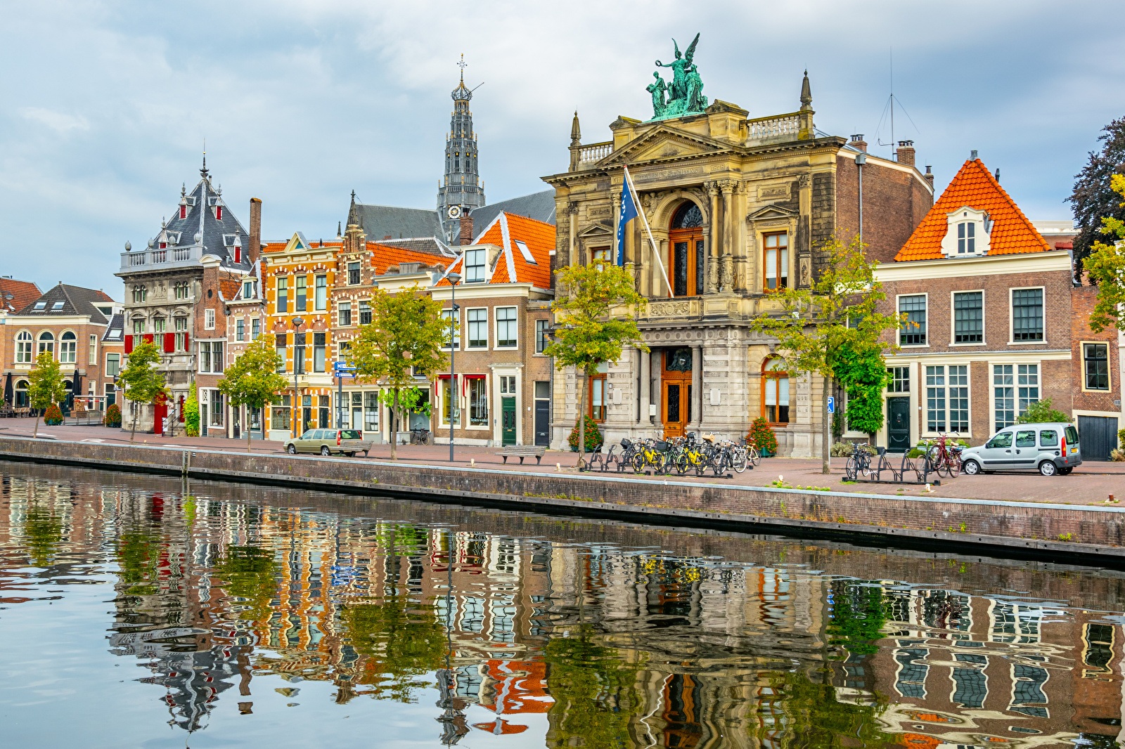 Historische gevels en het iconische Teylers Museum aan het Spaarne in Haarlem, met fietsen geparkeerd langs de kade en reflecties in het water