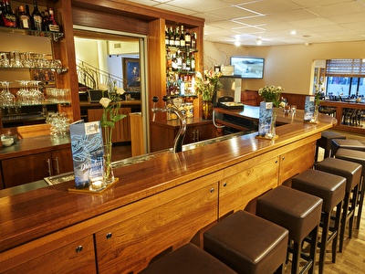 Atmospheric hotel bar in Amrâth Grand Hotel Frans Hals with wooden bar, comfortable bar stools and warm lighting.
