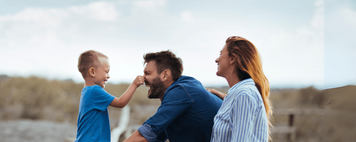 Lachende Familie mit Vater, Mutter und Kind, die zusammen Spaß in der Natur haben.