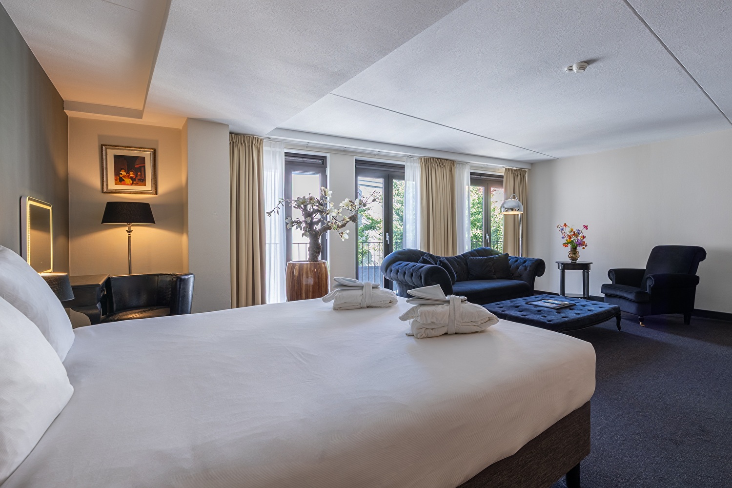 Junior Suite in Amrâth Grand Hotel Frans Hals with two single beds, a black fabric armchair, red patterned curtains, a mirror in the corner of the room, and art above the bed.