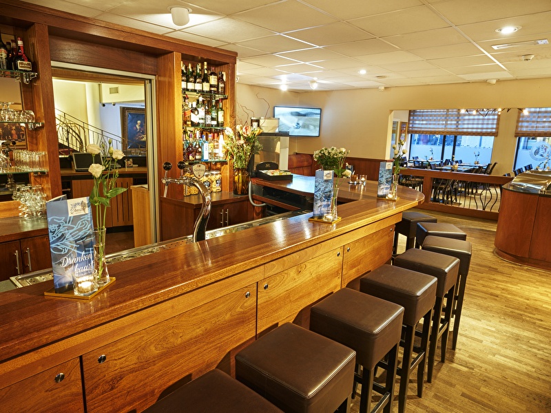 A wooden bar with bar stools and a few tables in Amrâth Grand Hotel Frans Hals.