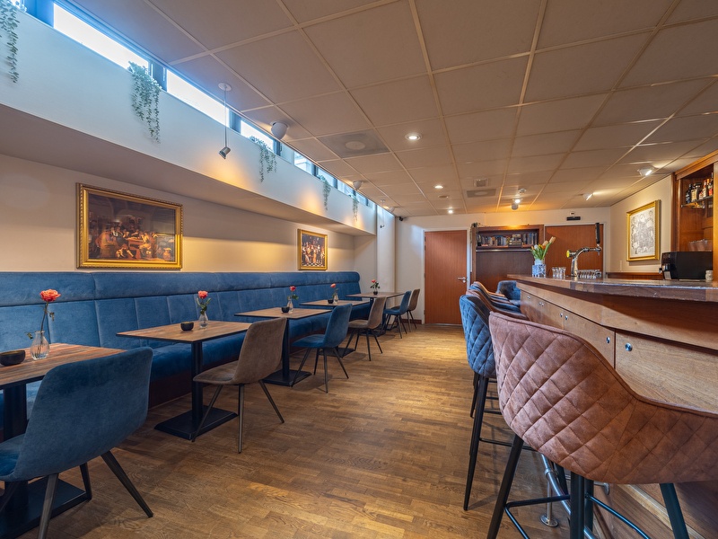 Eine Holztheke mit Barhockern und mehreren Tischen im Amrâth Grand Hotel Frans Hals.