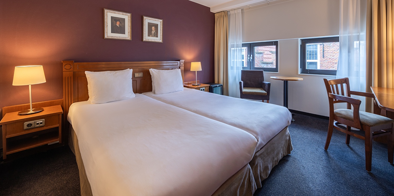 Deluxe Zimmer im Amrâth Grand Hotel Frans Hals mit zwei Einzelbetten, Nachttischlampen, zwei Gemälden über dem Bett und einem Holzkleiderschrank