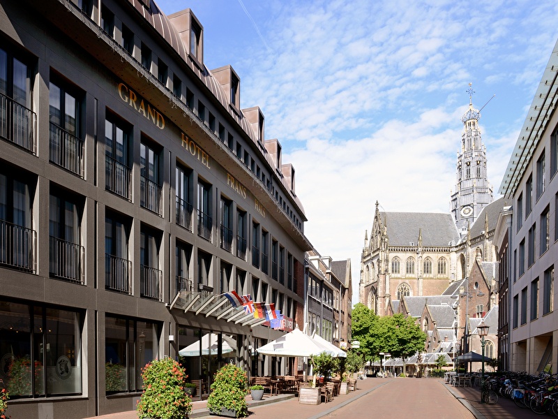  Vooraanzicht van Amrâth Grand Hotel Frans Hals in Haarlem, met de Grote Kerk (Sint-Bavokerk) zichtbaar aan het einde van de straat.