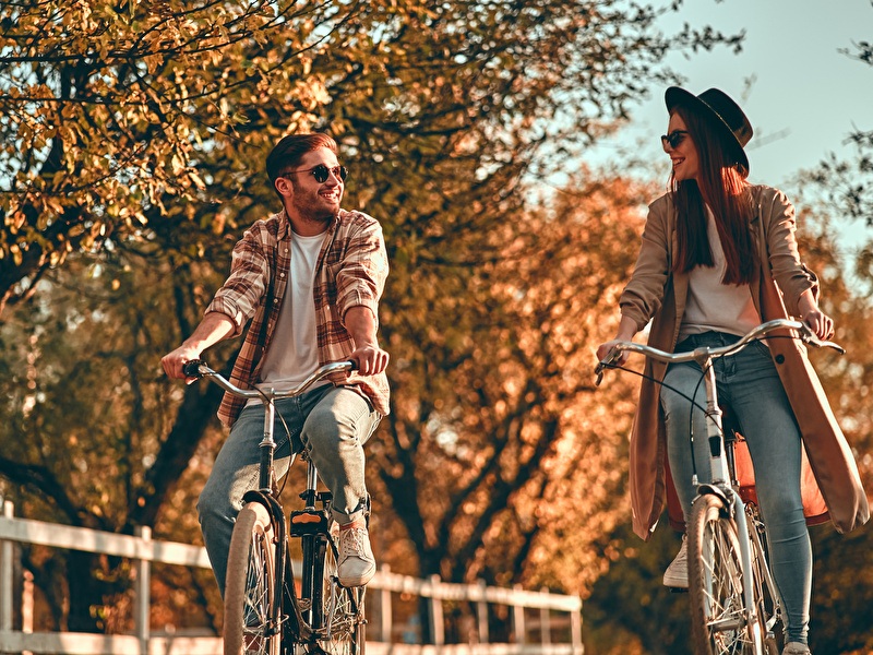 Man en vrouw fietsen lachend naast elkaar op een zonnige herfstdag.