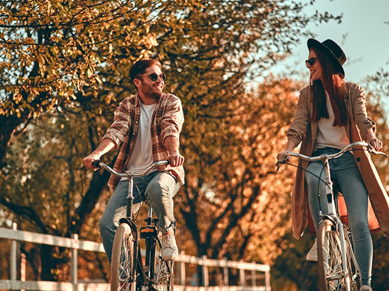 Man and woman are cycling, laughing side by side, on a sunny autumn day.