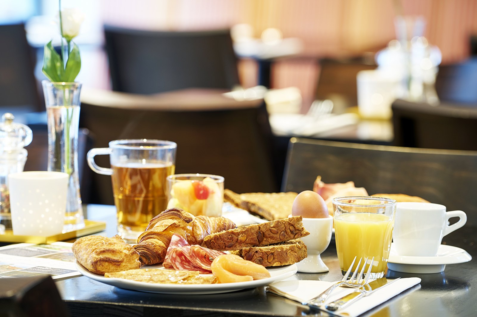 Ontbijttafel in Amrâth Grand Hotel Frans Hals met croissants, brood, vleeswaren, een gekookt ei, vers fruit, sinaasappelsap, koffie en thee.
