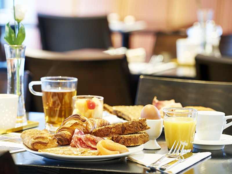 A breakfast plate with croissants, bread, cold cuts, salmon, a boiled egg, orange juice, and tea at Amrâth Grand Hotel Frans Hals.