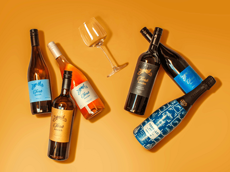 A selection of Amrâth Exclusives wine bottles, including red, white, and rosé wine, and an empty wine glass, lying on an orange background.