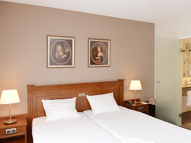 Deluxe room in Amrâth Grand Hotel Frans Hals features a twin bed with white sheets and pillows and two art objects on the wall
