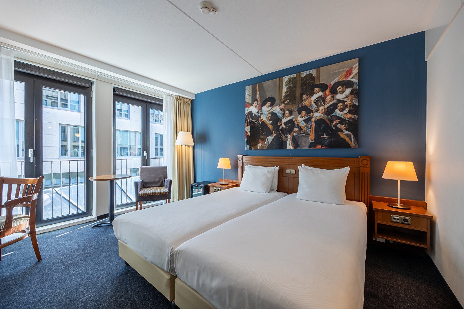Deluxe room in Amrâth Grand Hotel Frans Hals with two comfortable single beds, warm wooden accents, modern lighting, and a seating area by the window.