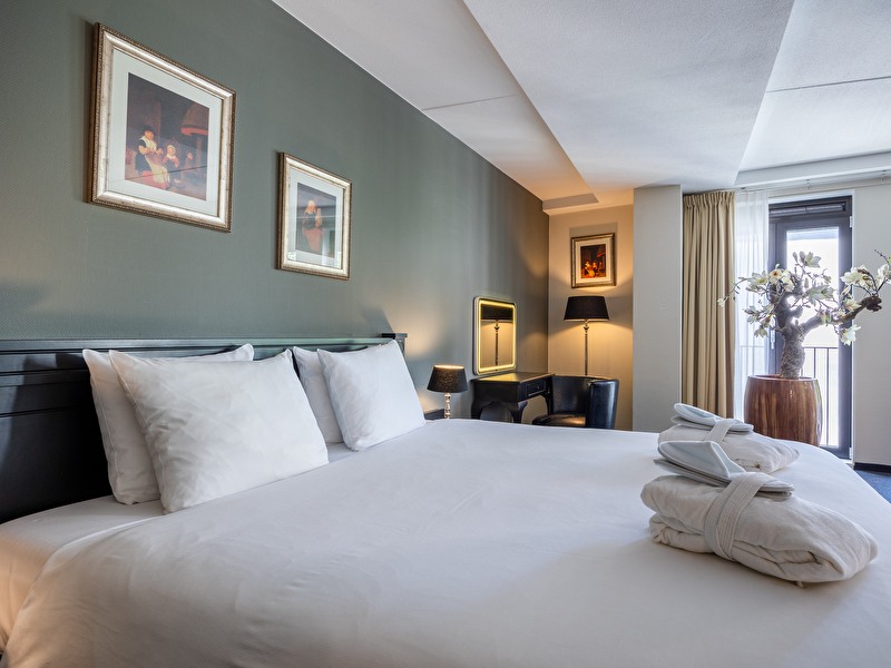 Junior Suite in Amrâth Grand Hotel Frans Hals met een groot tweepersoonsbed, rode gordijnen met bloemen, een zwarte bank en zwarte poef